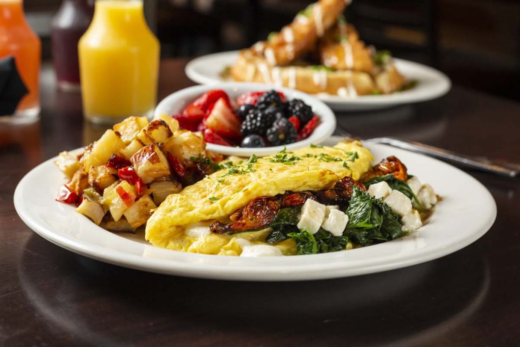 Omelet stuffed with mushrooms, cheese and spinach served with hashed browns, fruit cup in background