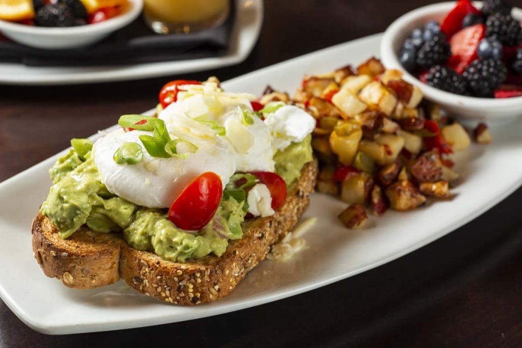 Avocado toast with hashed brown potatoes, fruit cup and breakfast juices in background