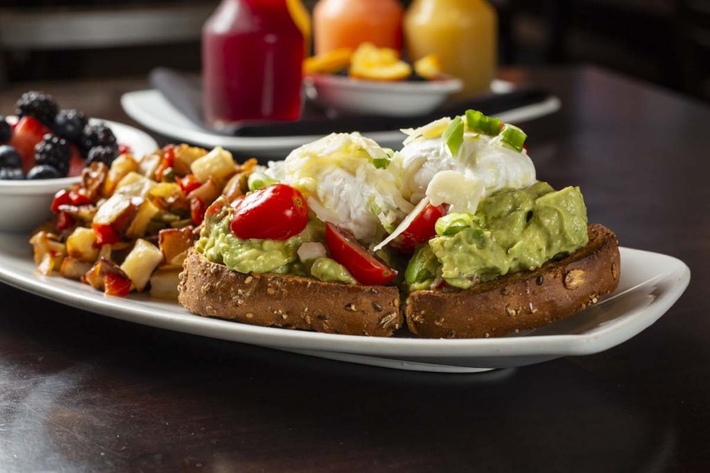 Avocado toast with hashed brown potatoes, fruit cup and breakfast juices in background