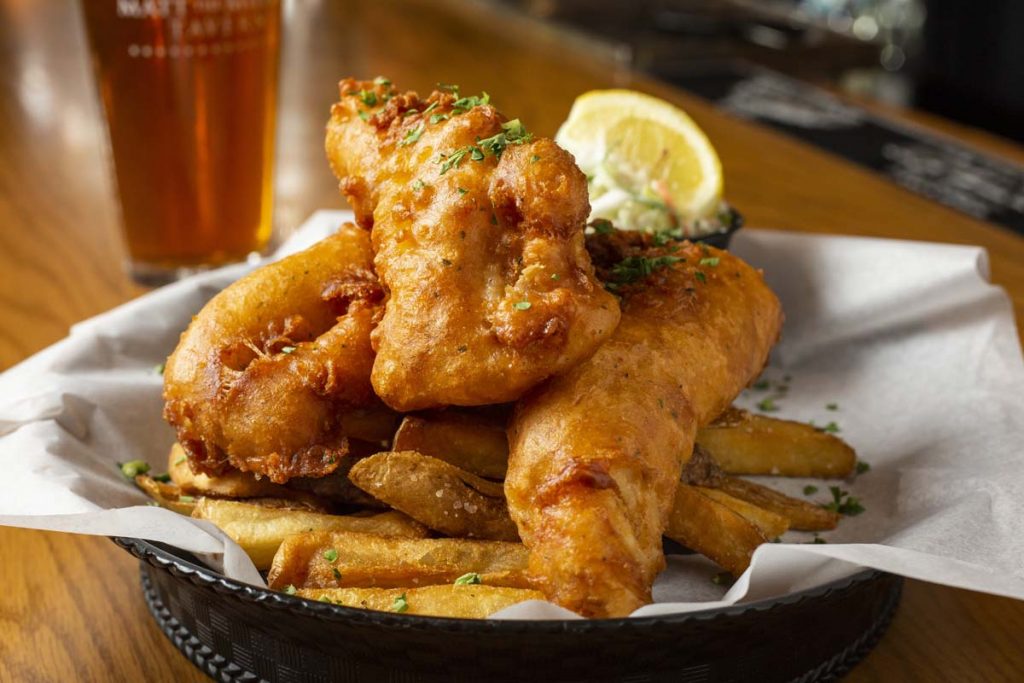 Three pieces of fried fish arranged on fries with lemon wedge