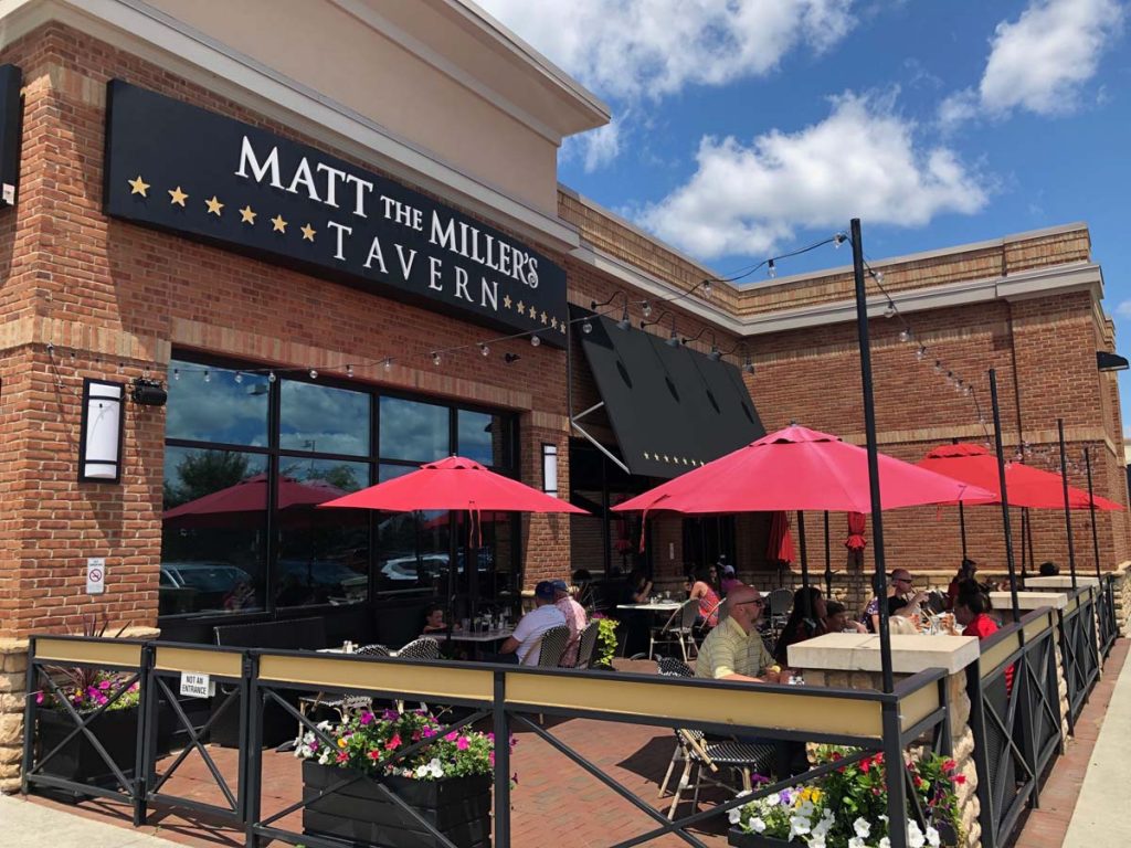 Exterior view of Matt the Miller’s patio with red umbrellas and seating at Gemini Place in Ohio