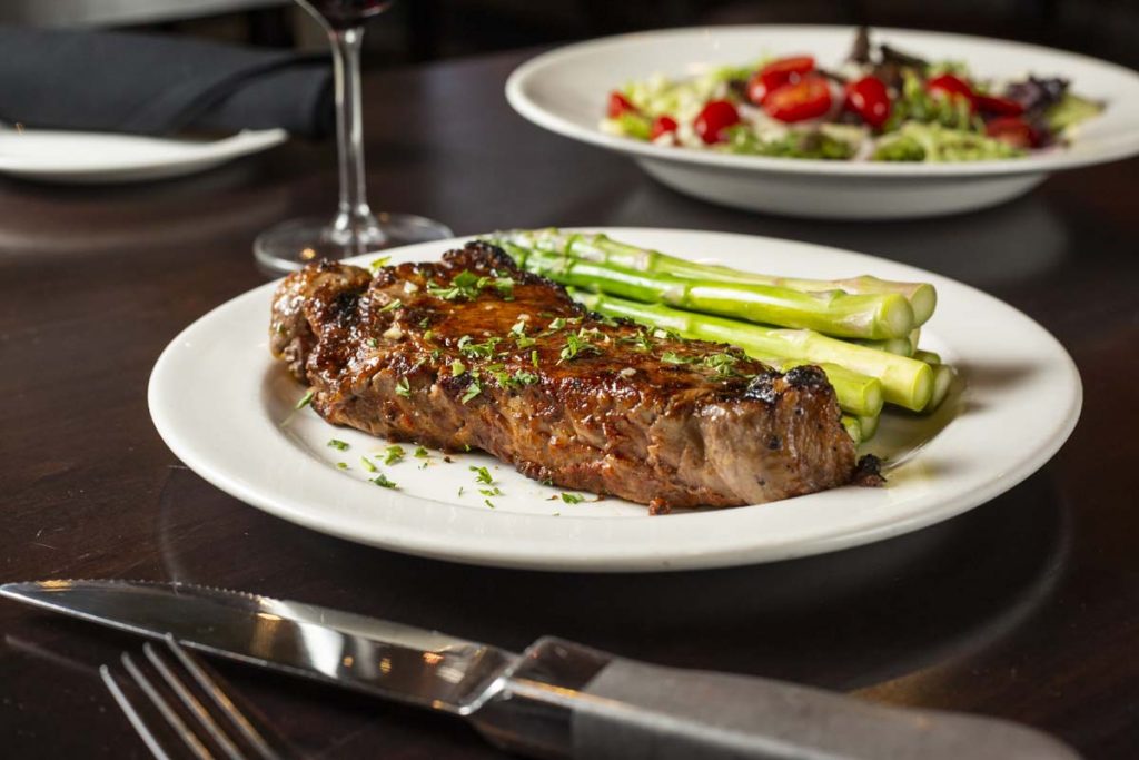 New York Strip Steak plated with asparagus and white wine with salad