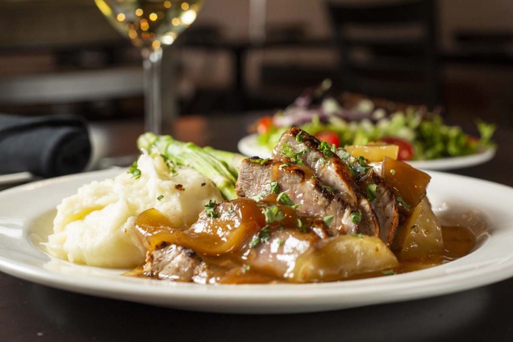 Plated roast pork entree with apple gravy and mashed potatoes with glass of white wine