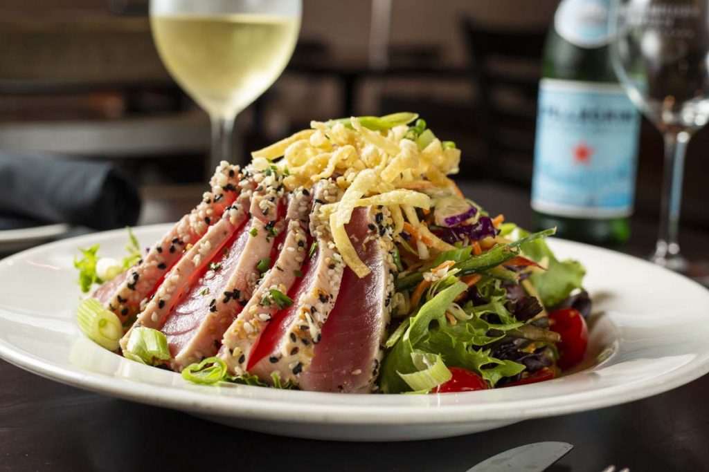 Seared Ahi Tuna slices plated on bed of lettuce with glass of white wine