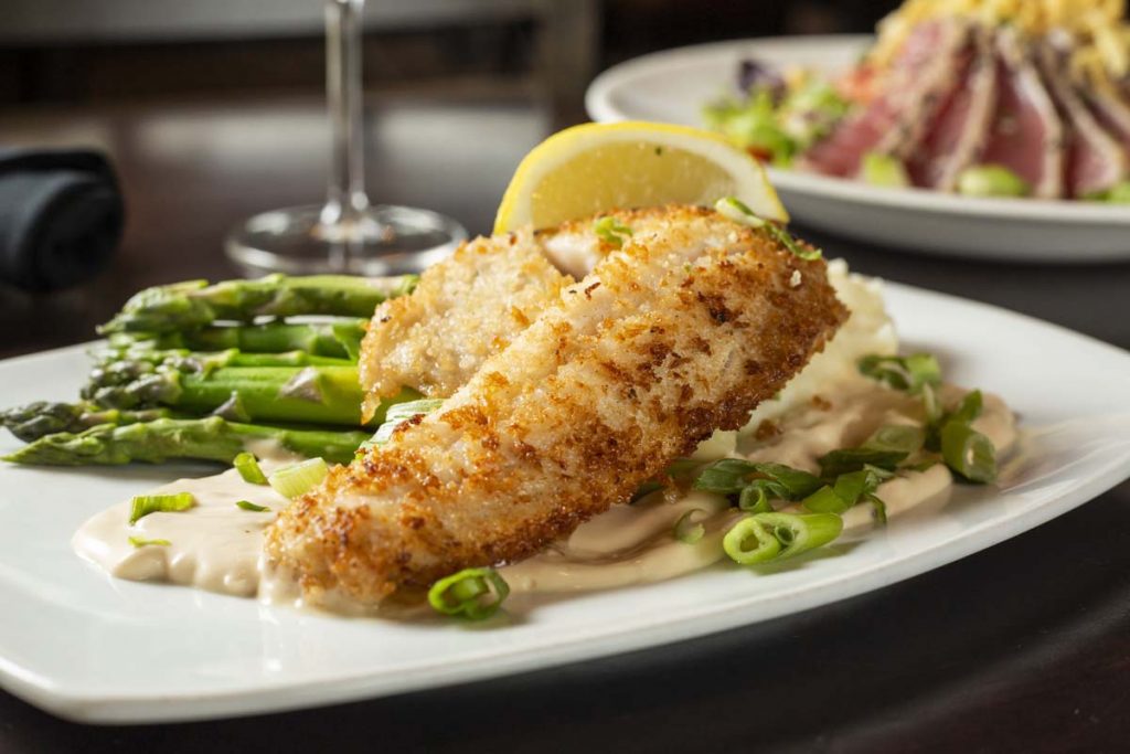 Plated walleye fish on potatoes with asparagus and glass of white wine