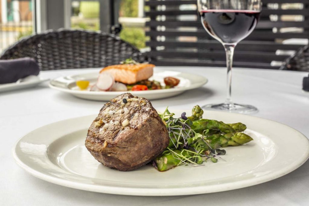 Piece of filet mignon steak plated with asparagus, glass of red wine in background